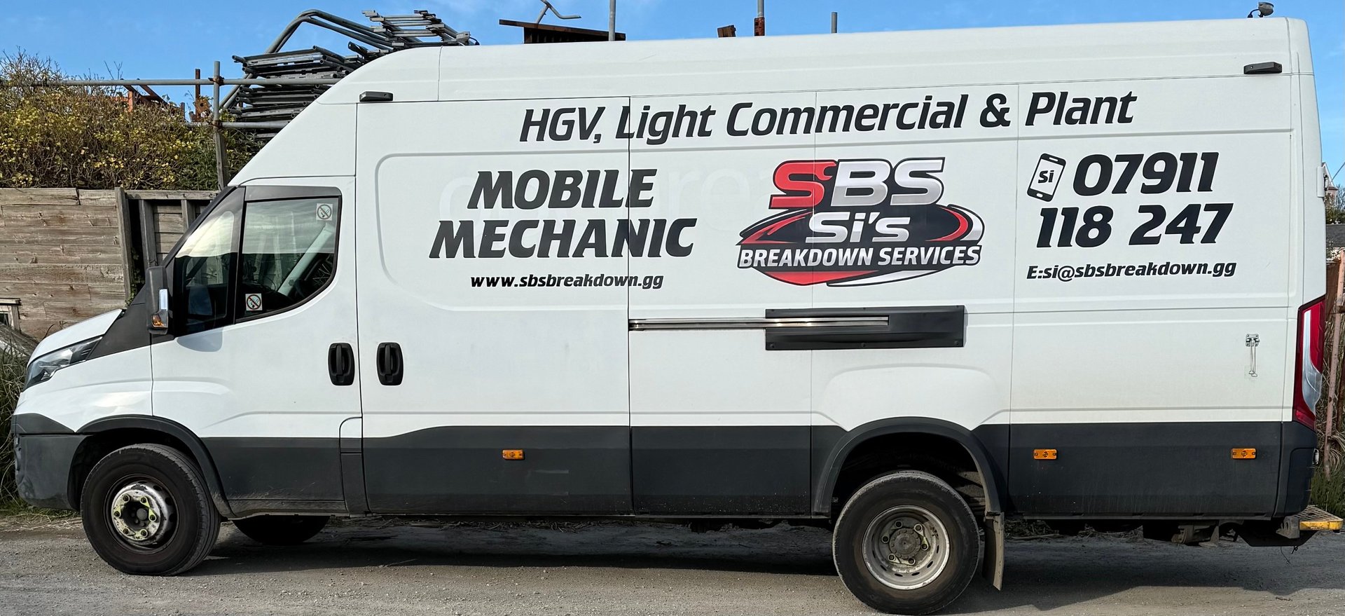 White and grey mobile mechanic van with equipment on roof rack and business contact details printed on the side