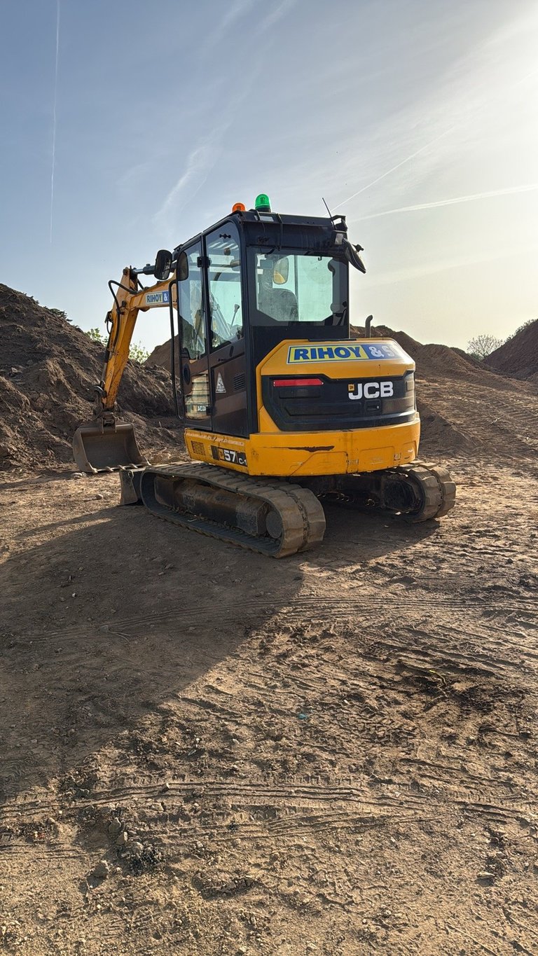 Yellow and black JCB mini excavator at a construction site with dirt piles and clear sky